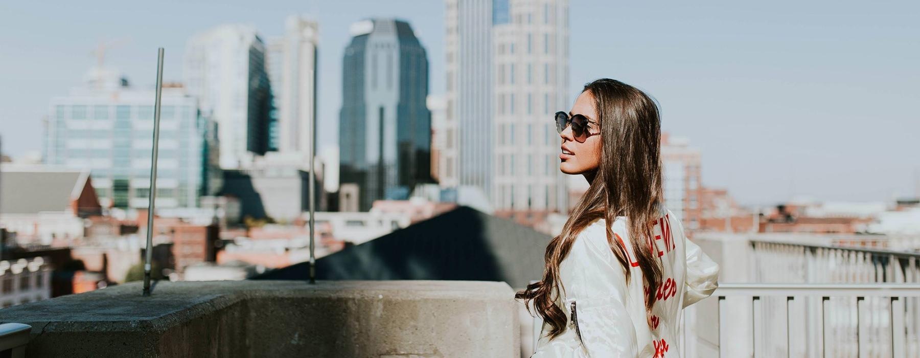 woman with sunglasses stands on a rooftop overlooking the city